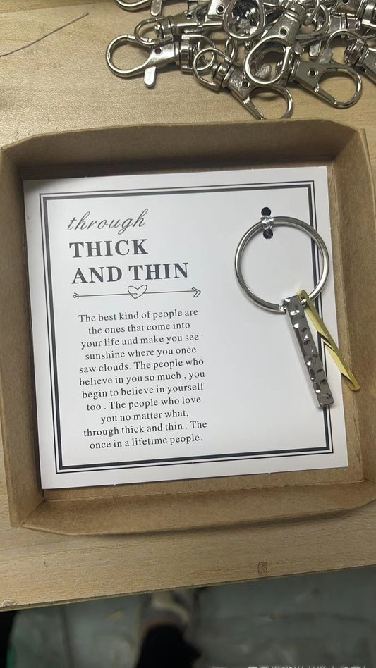 Keychain with round metal ring and ribbon tags resting on a card with printed quote.